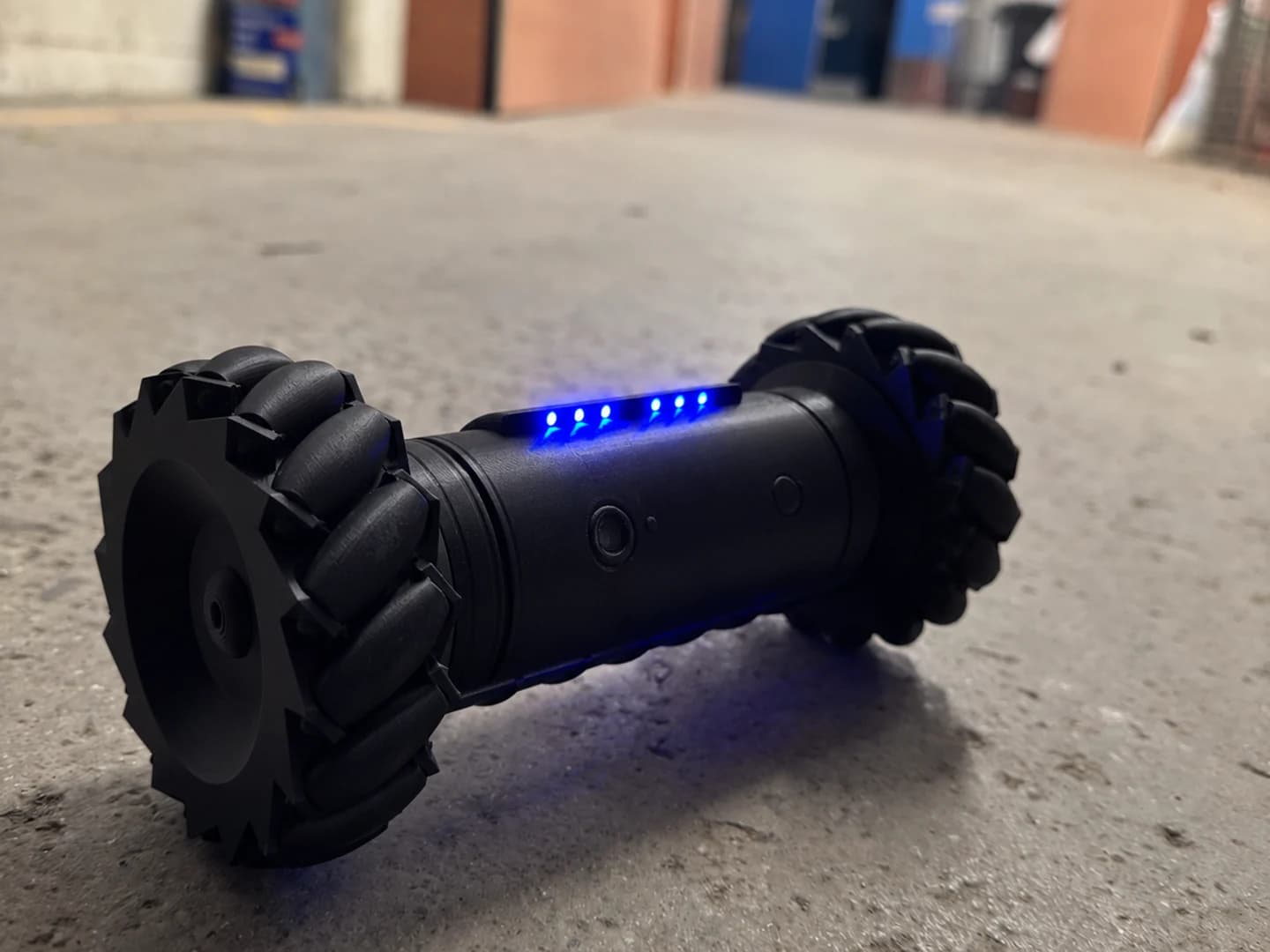 RCD-01 drone replica on a concrete corridor floor, seen from floor level with its six blue LEDs lit