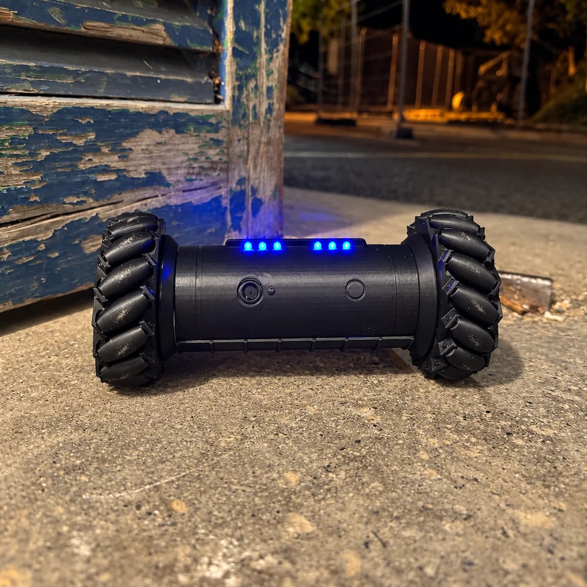 Front view of the RCD-01 drone replica at night: the lit LED bar, the lens and both treaded wheels